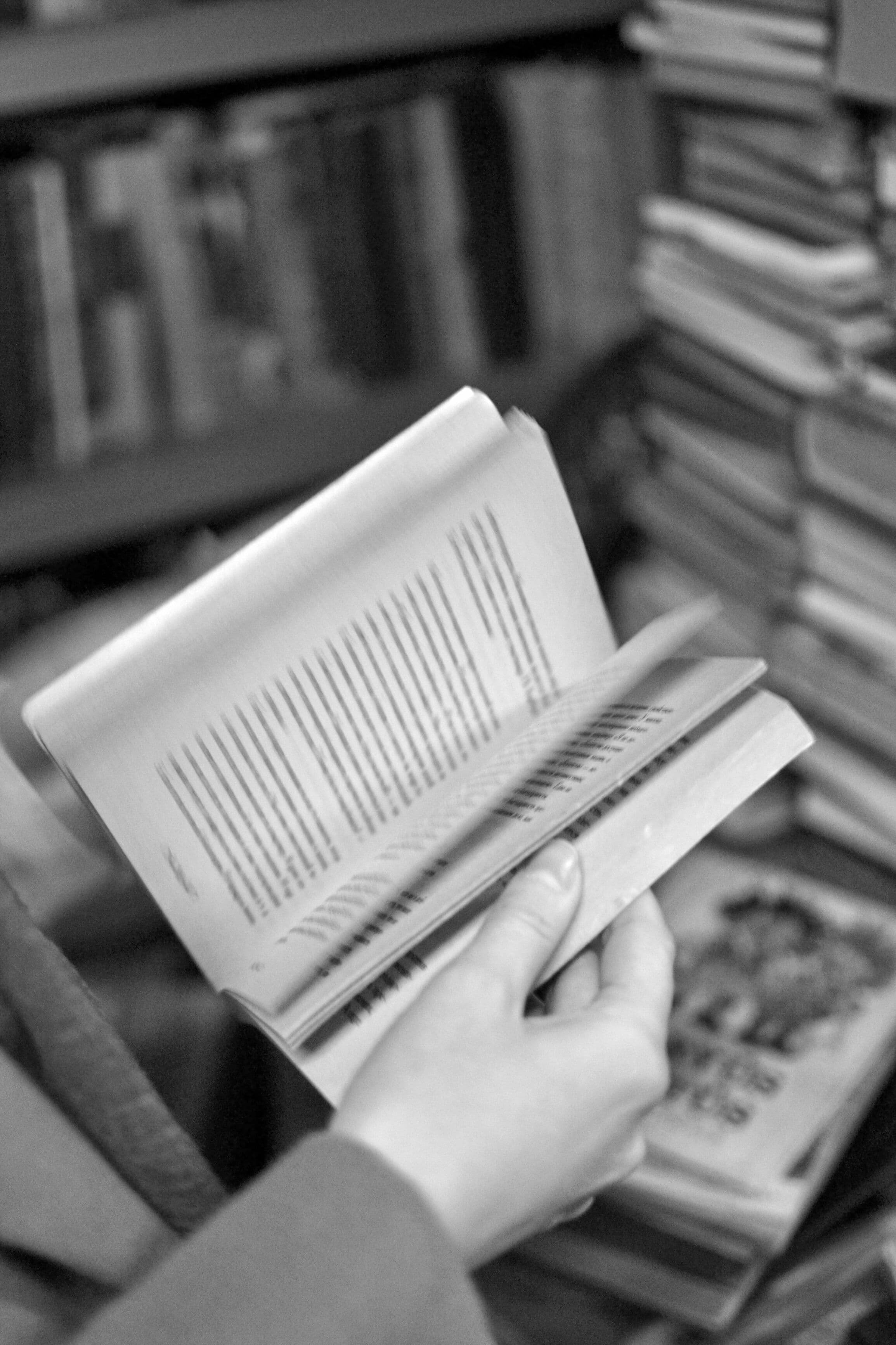 Mano sosteniendo un libro abierto frente a una biblioteca